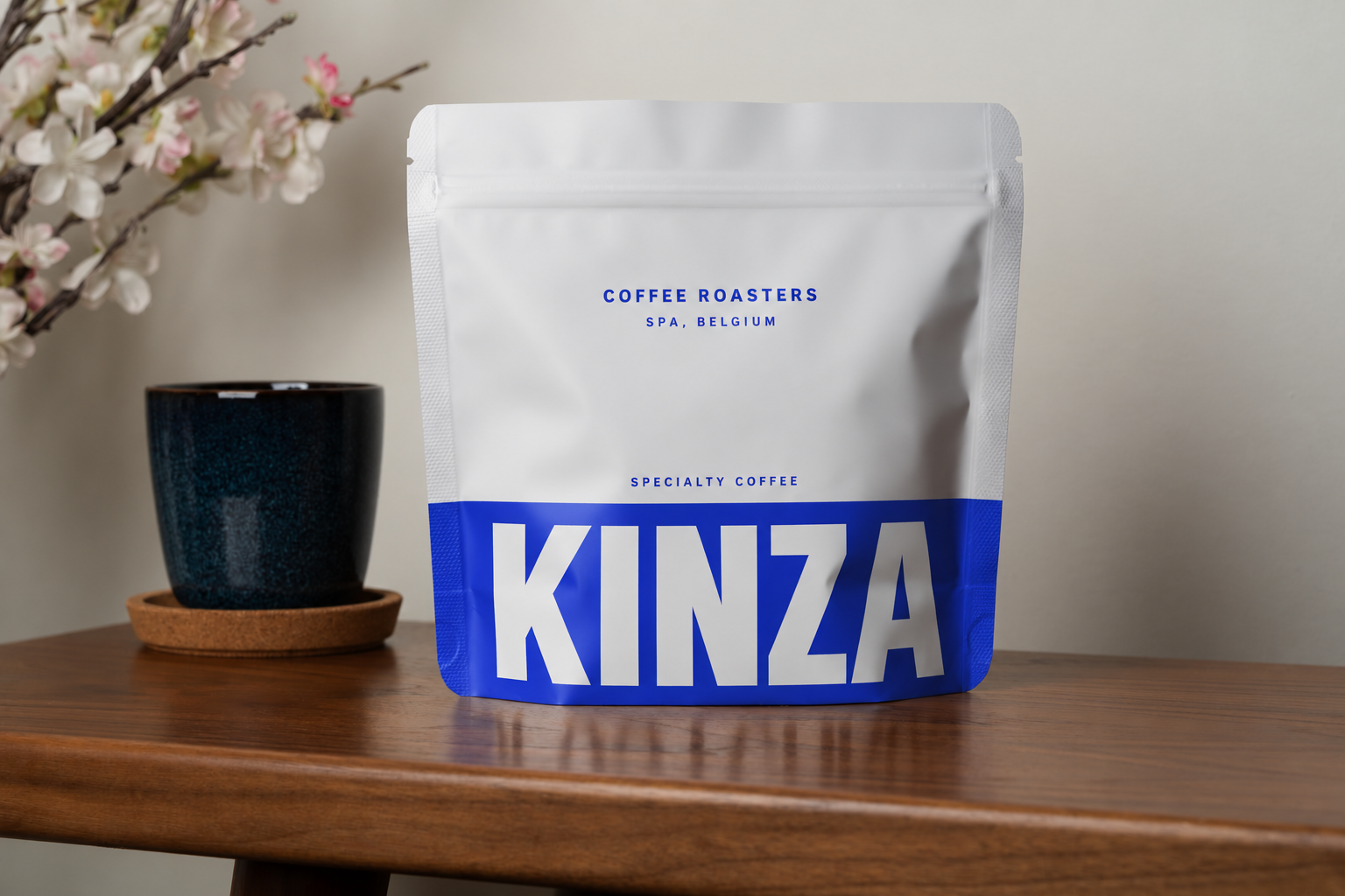 White and cobalt KINZA coffee pouch beside a ceramic coffee cup